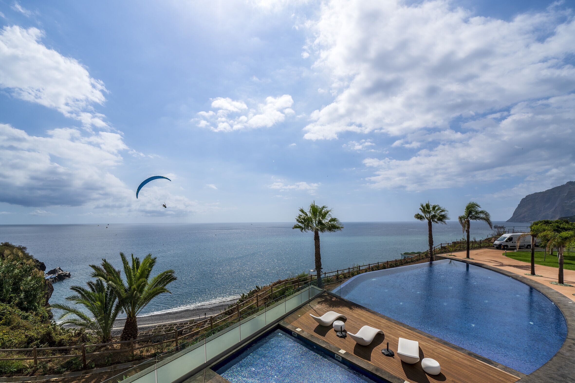 A pool with lounge chairs, a view of the ocean, and a parasail in the distance.