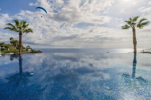 An infinity pool with palm trees, a clear sky, and a distant view of the ocean. - Luxury, elegance and sea view - Madeira Palace I (Funchal)