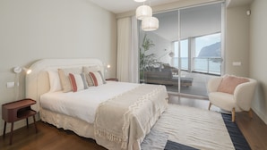 Une chambre à coucher avec un grand lit, des tables de chevet, une chaise, une fenêtre donnant sur un beau paysage et un luminaire au plafond.