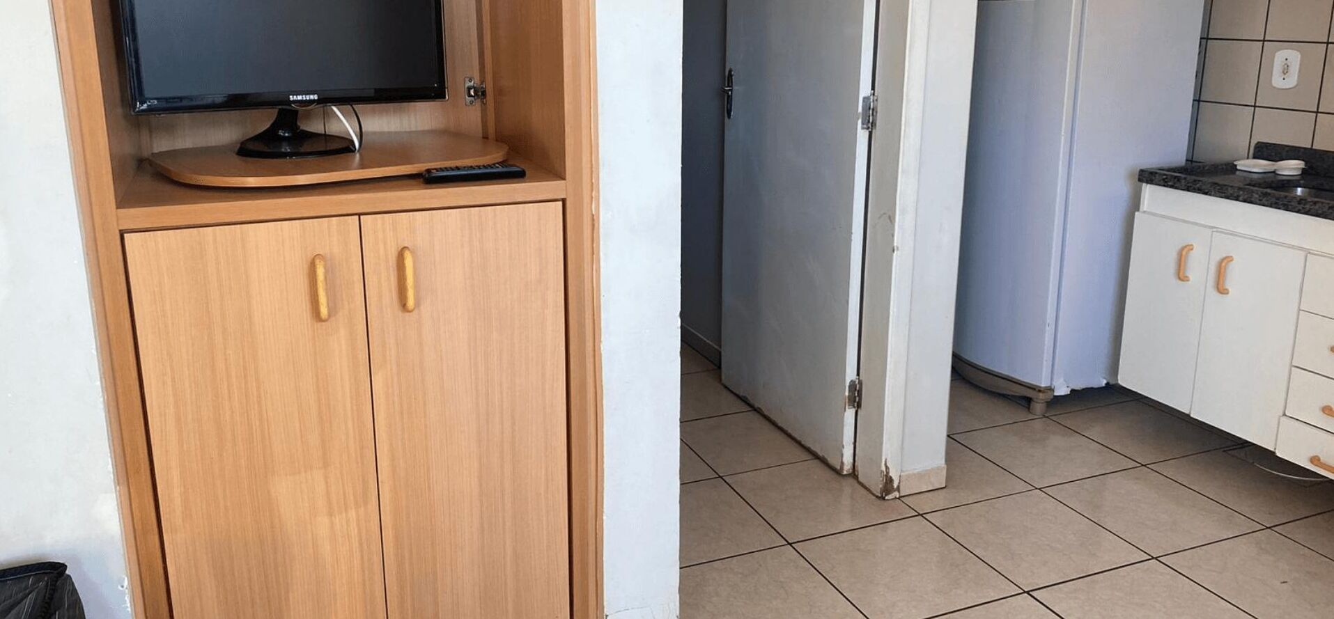 A kitchen with a refrigerator, cabinets, and a television on a wooden cabinet.