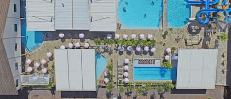 An aerial view of a resort with multiple swimming pools, a water slide, and beach umbrellas.