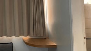 A small, single-bed room with a bedside table, a window with curtains, and a light fixture above the window. - Aptos - DiRoma Fiori - Aluguel Economico (Caldas Novas)