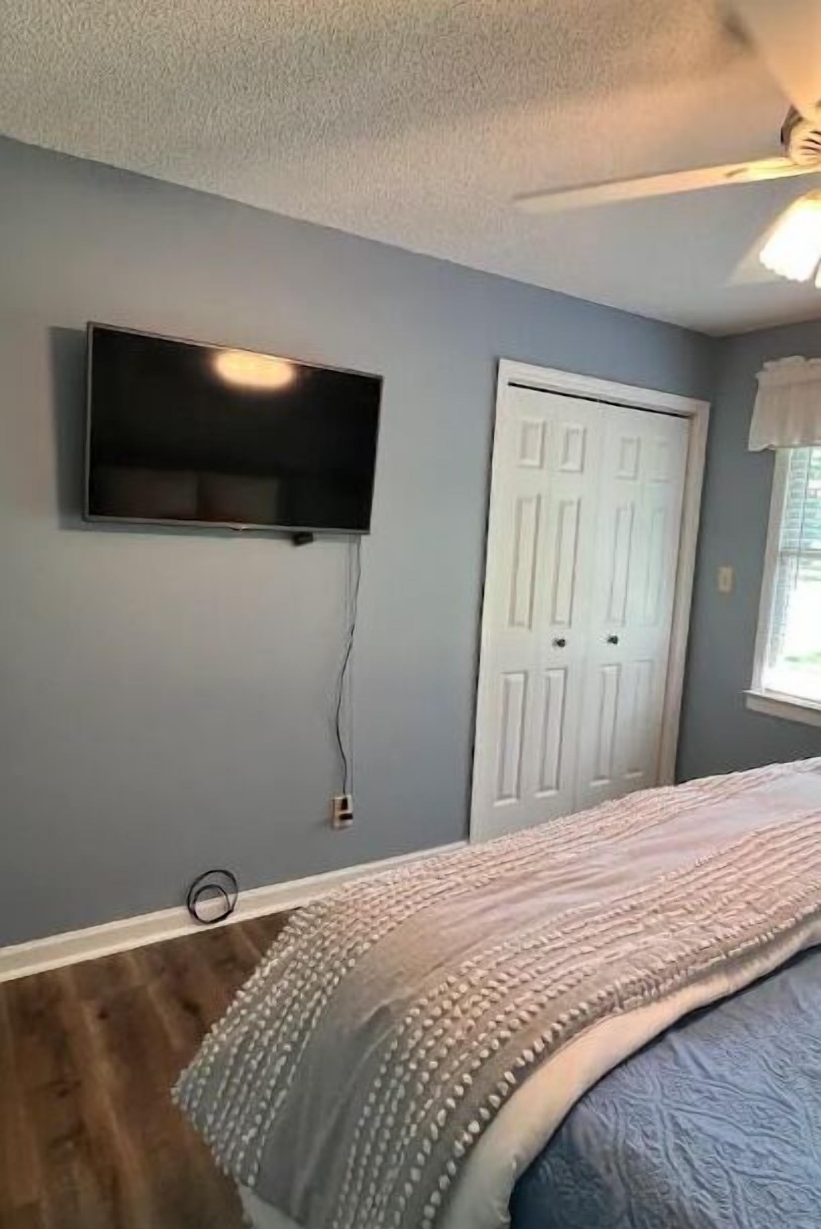 A bedroom with a bed, a television mounted on the wall, and a door.