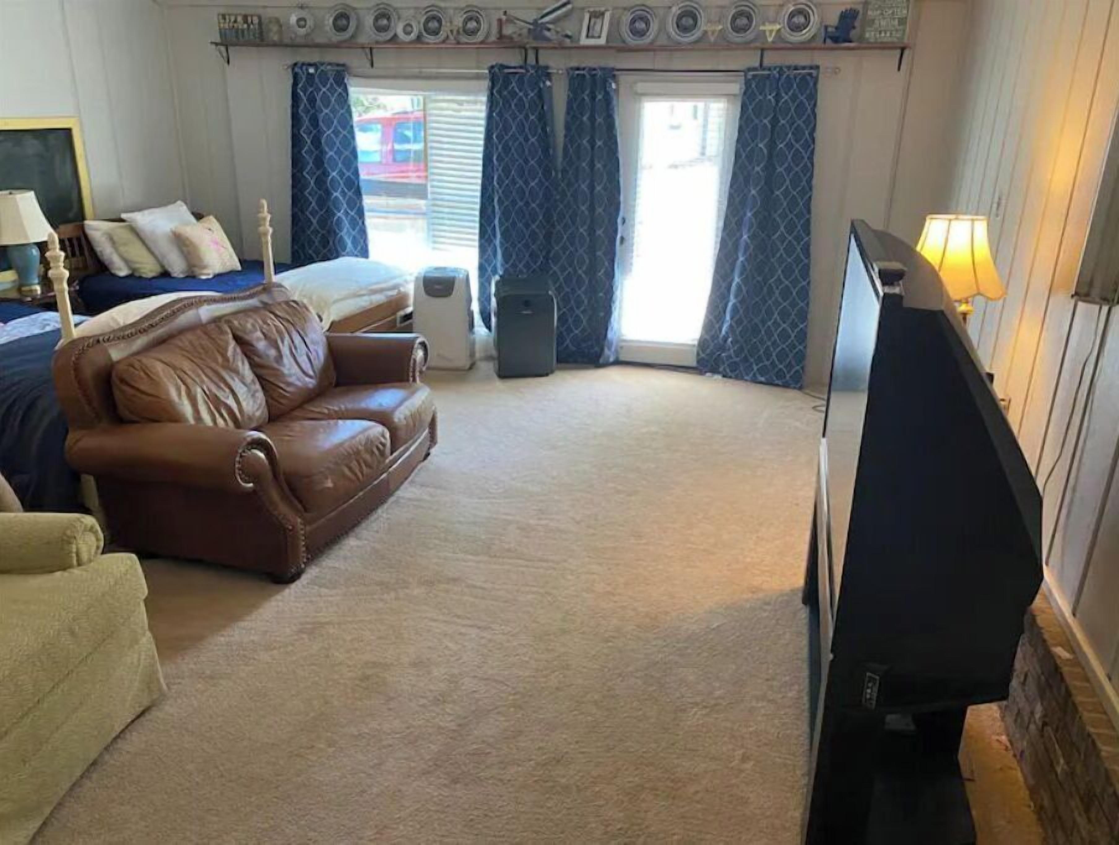 A hotel room with a brown leather sofa, a bed with blue bedding, a television, and a window with blue curtains.