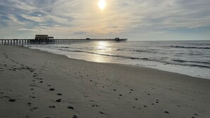 A beach with a pier extending into the ocean, featuring a building with a flat roof and a flagpole.