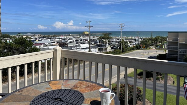 A balcony with a table, a cup, and a view of a marina with boats and a beach.