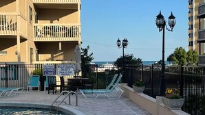 A swimming pool area with lounge chairs, a lifeguard sign, and a view of the sea.