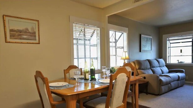 Un comedor con una mesa y sillas de madera, un sofá y una ventana con persianas.