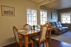 Un coin repas avec une table et des chaises en bois, un canapé et une fenêtre avec des stores.