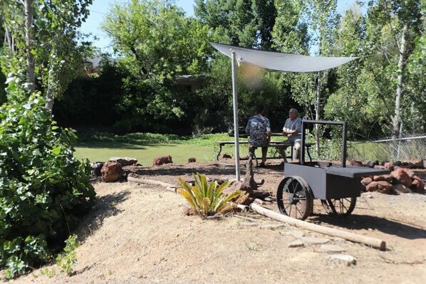 Un chariot doté d’un auvent, situé dans un espace jardin avec des arbres et un étang.