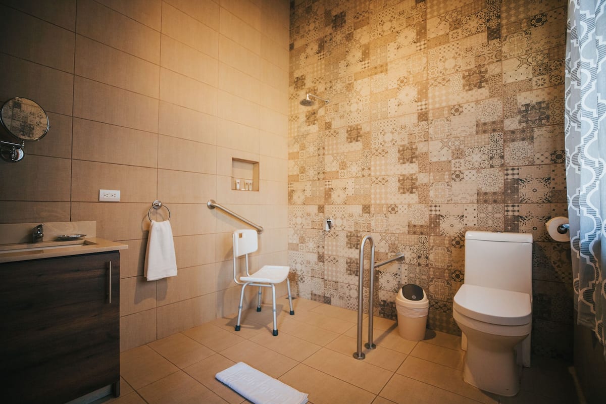A bathroom with a shower, toilet, sink, and a chair.
