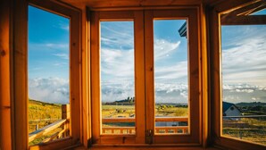 A wooden room with large windows offering a view of a rural landscape, including fields and a distant building. - Cabañas & Mirador Secret Garden Costa R. (Potrero Cerrado)
