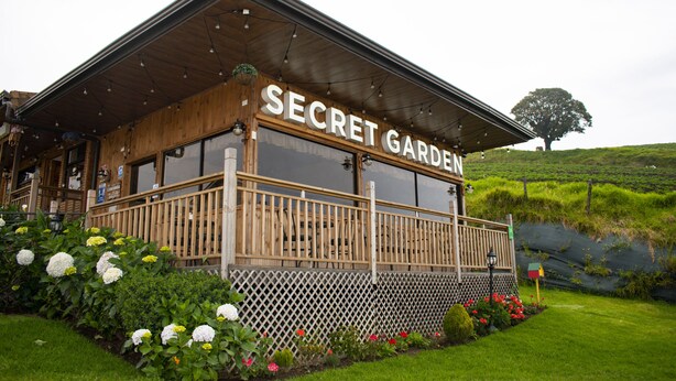 A wooden building with a sign reading "SECRET GARDEN." It has a wooden deck and is surrounded by greenery and flowers. - Cabañas & Mirador Secret Garden Costa R. (Potrero Cerrado)
