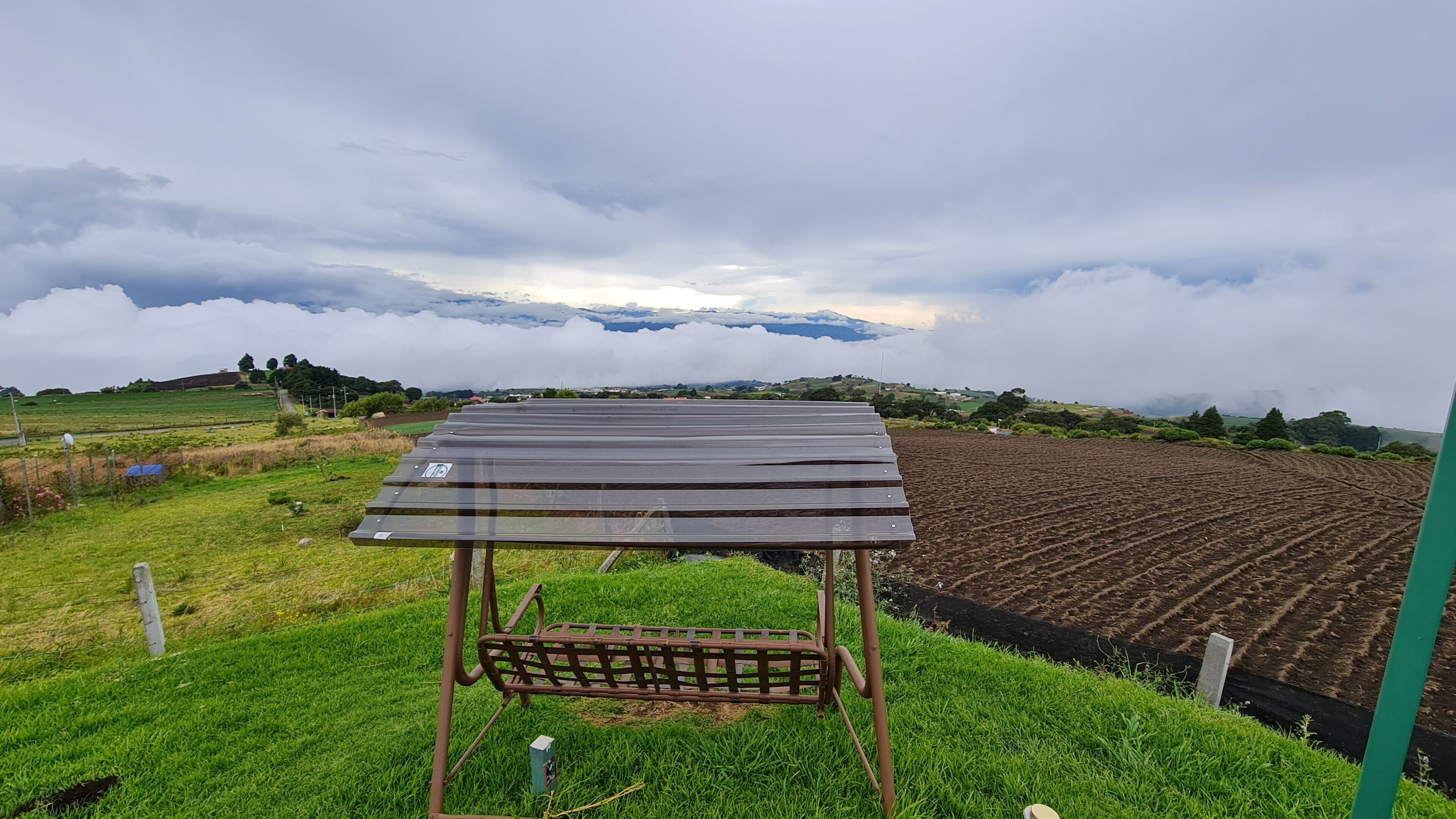 A solar panel installation on a grassy field with a view of a cultivated field and distant mountains.