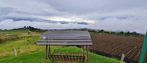A solar panel installation on a grassy field with a view of a cultivated field and distant mountains.