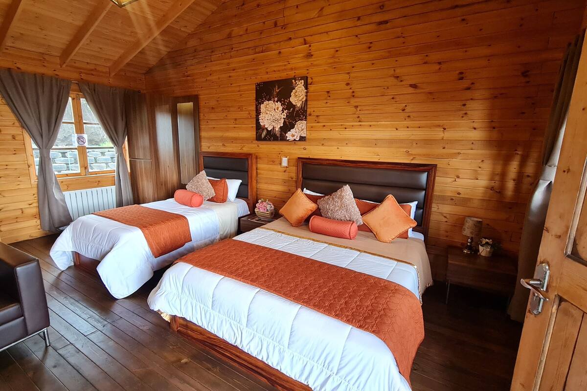 A wooden cabin room with two beds, a sofa, and a painting on the wall.