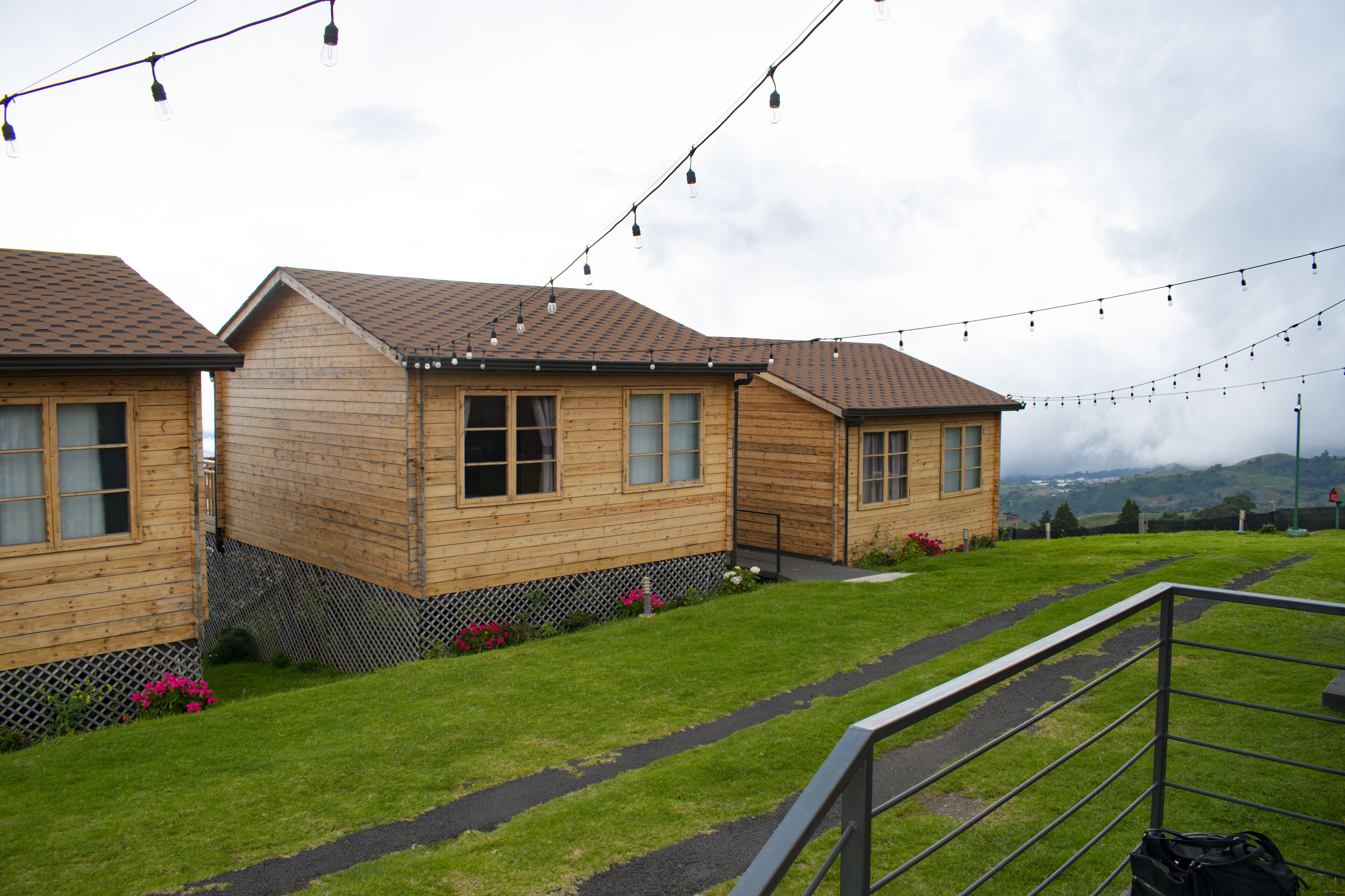 A row of wooden cabins with a grassy lawn and a metal railing in the foreground.