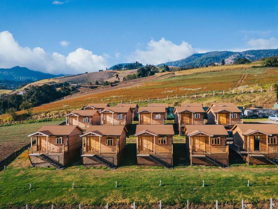 A row of wooden cabins with a view of rolling hills and a clear sky.