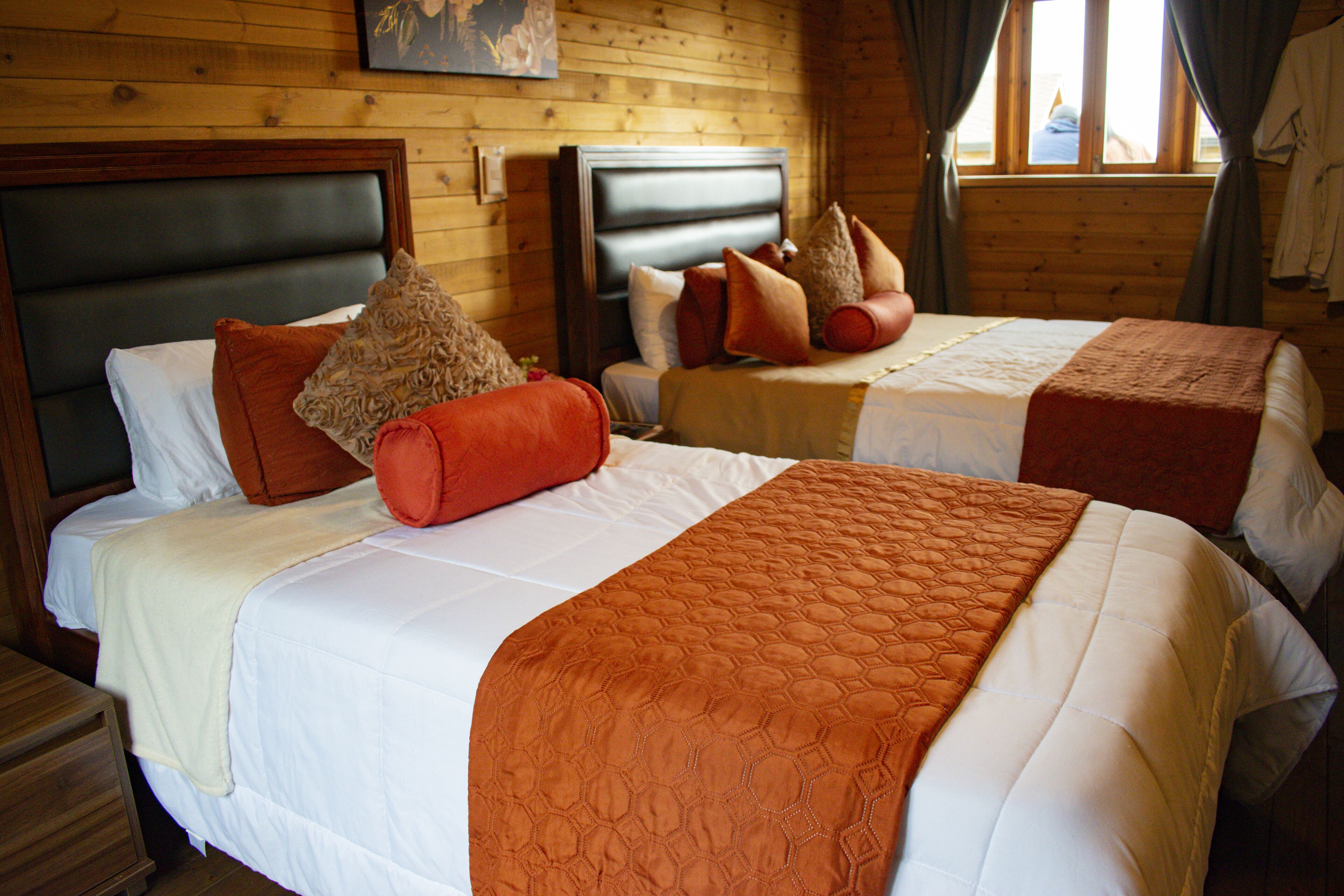 Two double beds with headboards, a wooden wall, and a window with curtains.