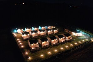 Reihenweise angeordnete, gleichmäßig beleuchtete Hütten mit eingezäunter Fläche, was auf einen Urlaubsort oder Campingplatz hindeutet.