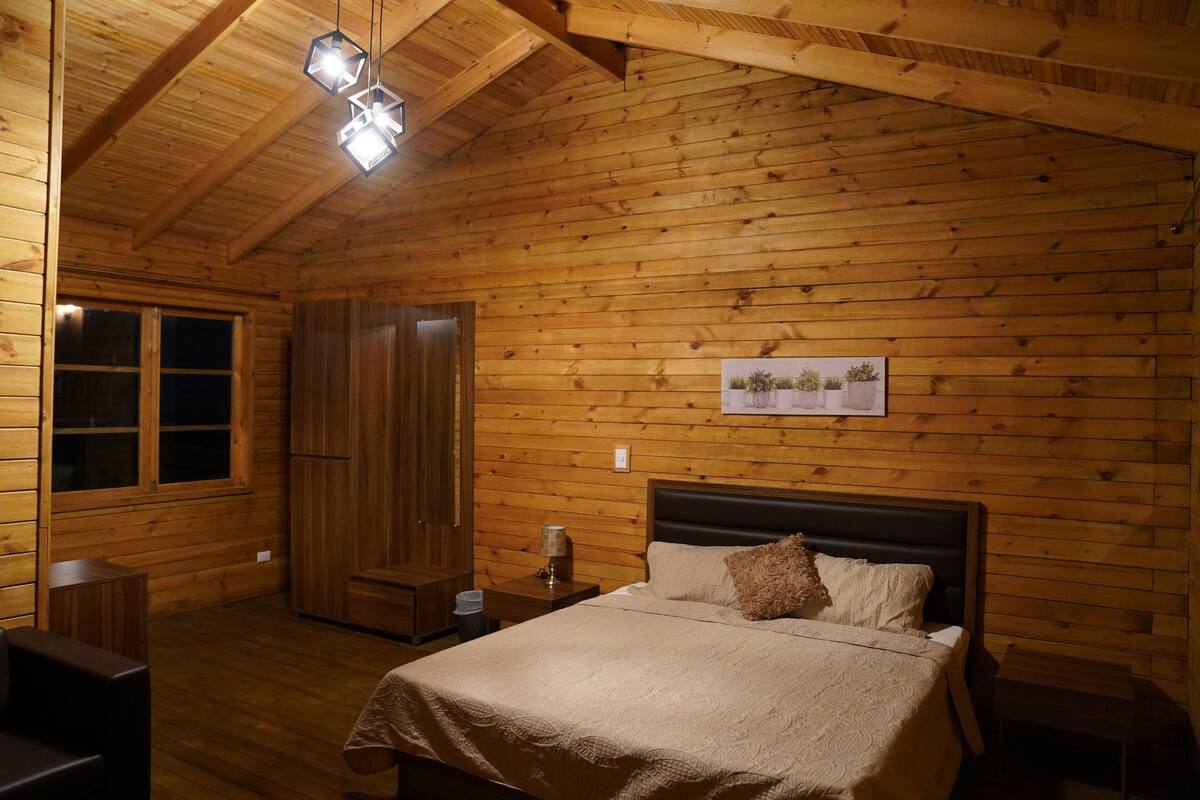 A wooden-paneled room with a bed, a nightstand, a lamp, and a framed picture on the wall.