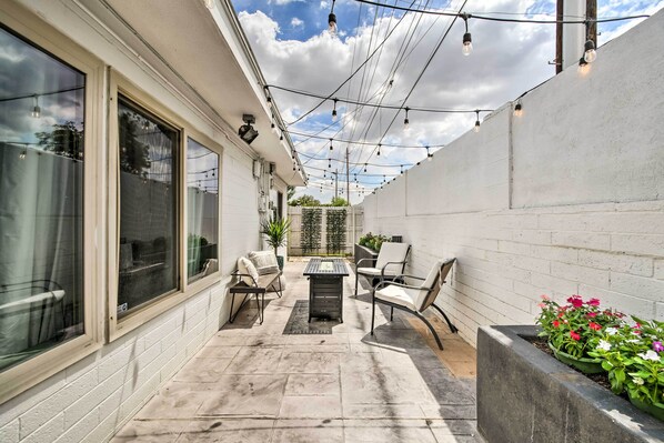 Relax in a patio with a clean design, featuring a table and chairs, surrounded by a brick wall and lush greenery.