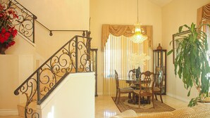 A staircase with ornate metal railings, a dining area with a chandelier, and a large potted plant. - Tranquil 4BR/3BA private house w/ inviting yard perfect for any type of stay (Fontana)