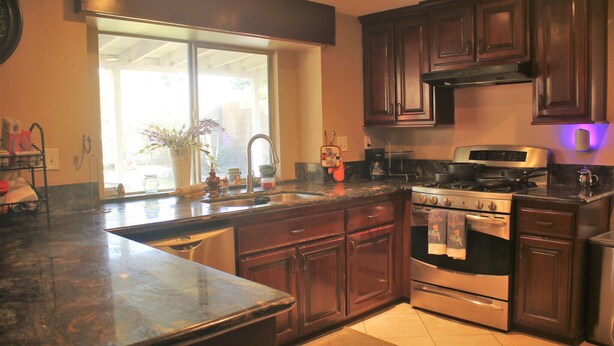 A kitchen with dark wooden cabinets, a stainless steel stove, and a large window providing natural light. - Tranquil 4BR/3BA private house w/ inviting yard perfect for any type of stay (Fontana)
