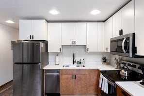 Una cocina moderna con electrodomésticos de acero inoxidable, armarios blancos y encimera negra.
