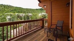 Een houten balkon met uitzicht op een bebost heuvel en huizen.