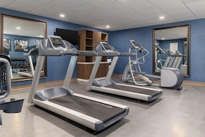 A gym with treadmills, a mirrored wall, and a blue wall with framed pictures. - 1 Bedroom | Heated Outdoor Pool + Free Breakfast (Chandler)