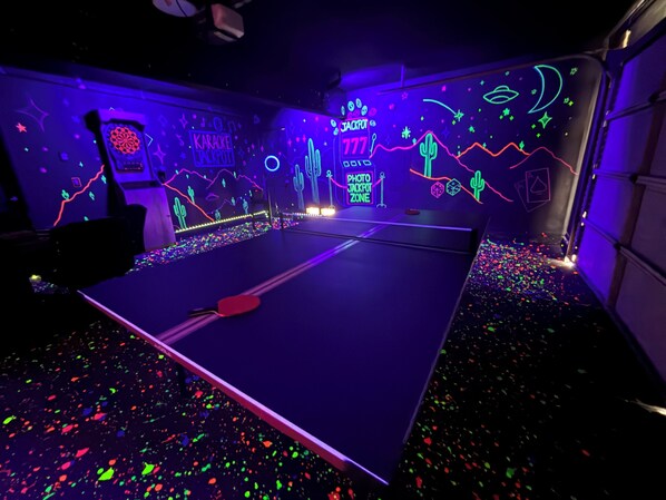 A room with a ping pong table, neon signs, and a starry wall design.