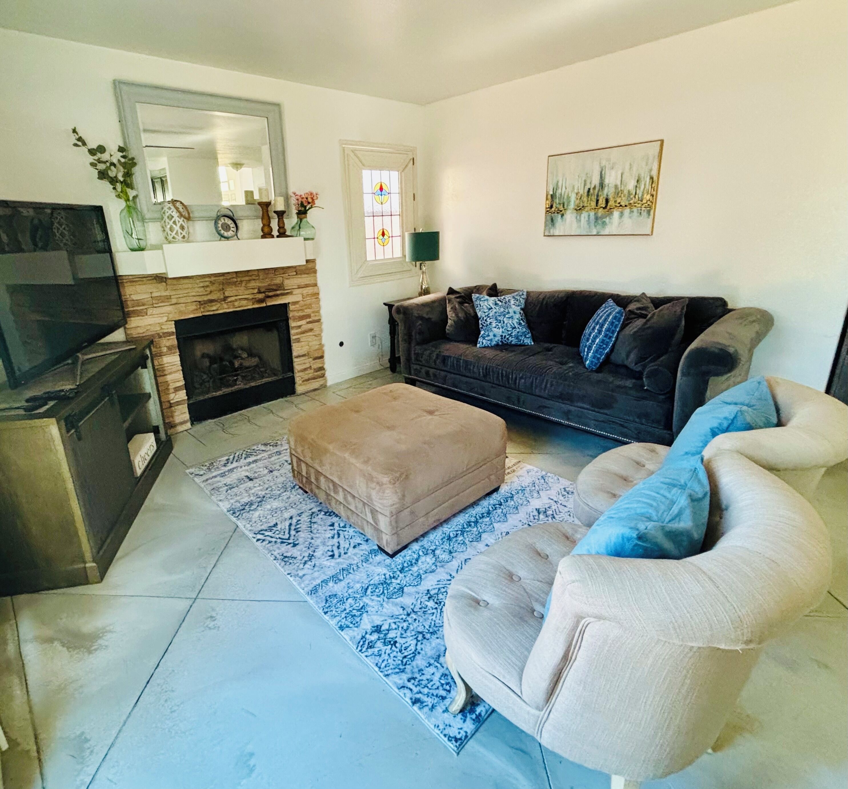Una sala de estar con chimenea, un sofá, un reposapiés y un televisor.