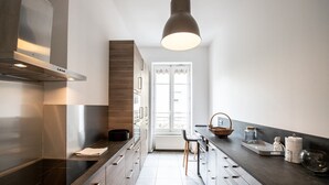 A modern kitchen with a central island, a built-in stove, and a large window providing natural light. - 128 Thiers (Villeurbanne)