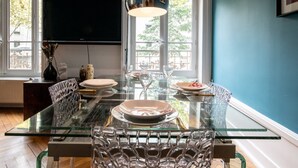 A modern dining area with a glass table, clear glass chairs, and a flat-screen TV mounted on the wall. - 128 Thiers (Villeurbanne)