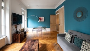 A living room with a teal wall, wooden flooring, a gray sofa, a coffee table, and a TV on a wooden stand. - 128 Thiers (Villeurbanne)