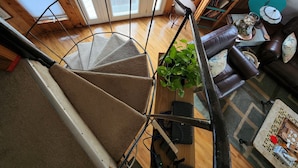 Una escalera de caracol en un interior de madera con vista a una sala de estar inferior.