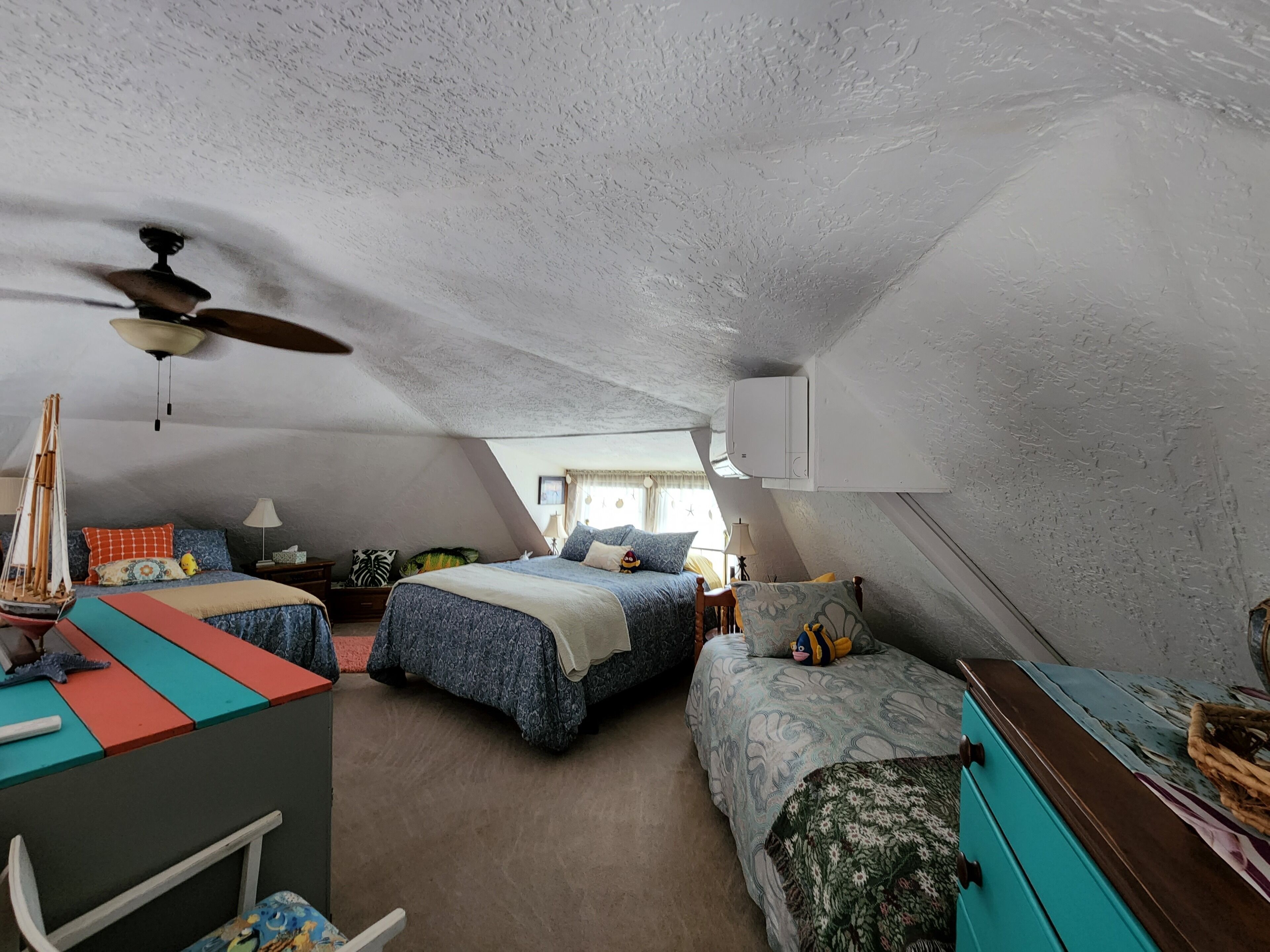 Un dormitorio acogedor en el ático con dos camas, un escritorio y un ventilador de techo.
