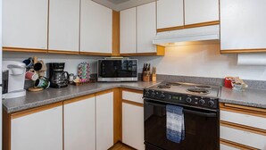 Une cuisine avec des armoires blanches, une cuisinière, un four à micro-ondes et divers ustensiles de cuisine sur le plan de travail.
