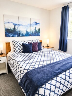 Une chambre à coucher avec un grand lit, une table de chevet, une lampe et un tableau représentant une forêt accroché au mur.