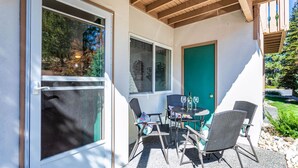 Une terrasse couverte avec une table et des chaises, une porte et une fenêtre donnant sur un jardin.