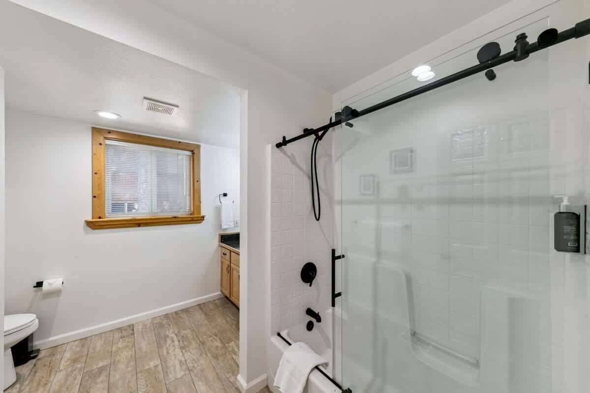 Een badkamer met toilet, douche met glazen deur, raam met zonwering en een handdoekrek.