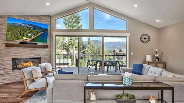 A modern living room with a fireplace, large windows, a flat-screen TV, and a dining area. - Mountain Base Camp: Hot Tub, A/C, Dog Friendly (South Lake Tahoe)