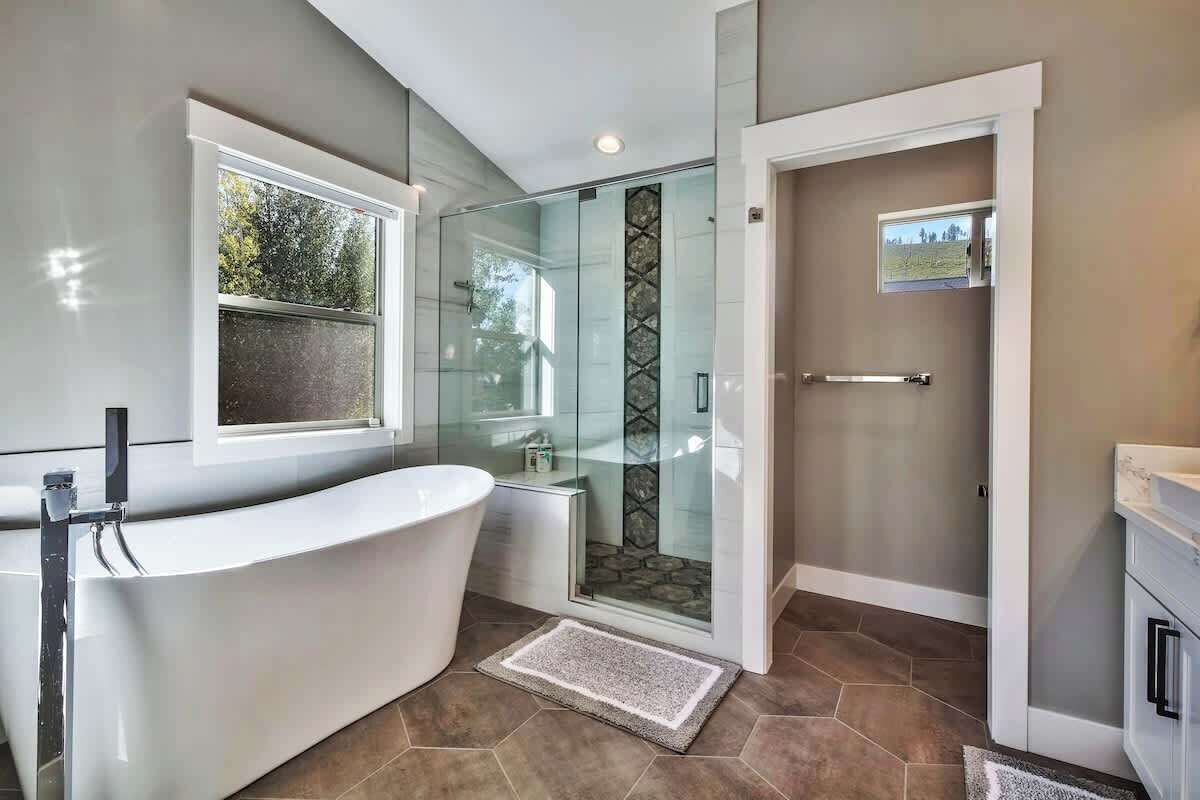 A modern bathroom with a freestanding bathtub, a glass-enclosed shower, and a view of the outdoors.