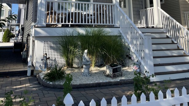 A two-story house with a front porch, a staircase, and a small garden area with a bird statue. - Mermaid Place is only 5 min walk to the beach. (Seaside Heights)