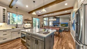 A modern kitchen with a large island, wooden beams, pendant lights, and a built-in refrigerator. - PeakViewTahoe: Hot Tub, AC, Game Room, ProjectorTV (South Lake Tahoe)