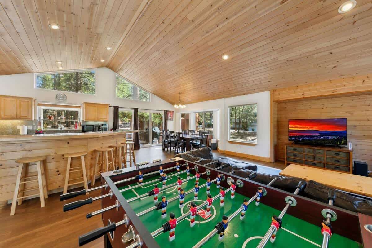 Una habitación amplia con mesa de fútbol, techo de madera y ventanas grandes.