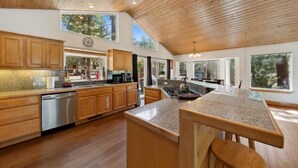 A modern kitchen with wooden cabinets, stainless steel appliances, and large windows.