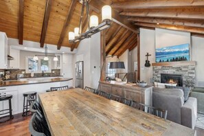 Een ruime keuken met een grote houten tafel, barstoelen en een stenen openhaard.