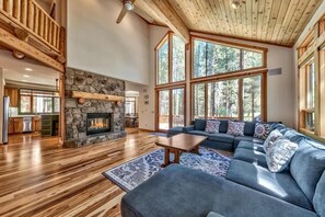 Ein großzügiges Wohnzimmer mit Kamin aus Stein, großen Fenstern, Holzbalkendecke und einem modernen Sofa.